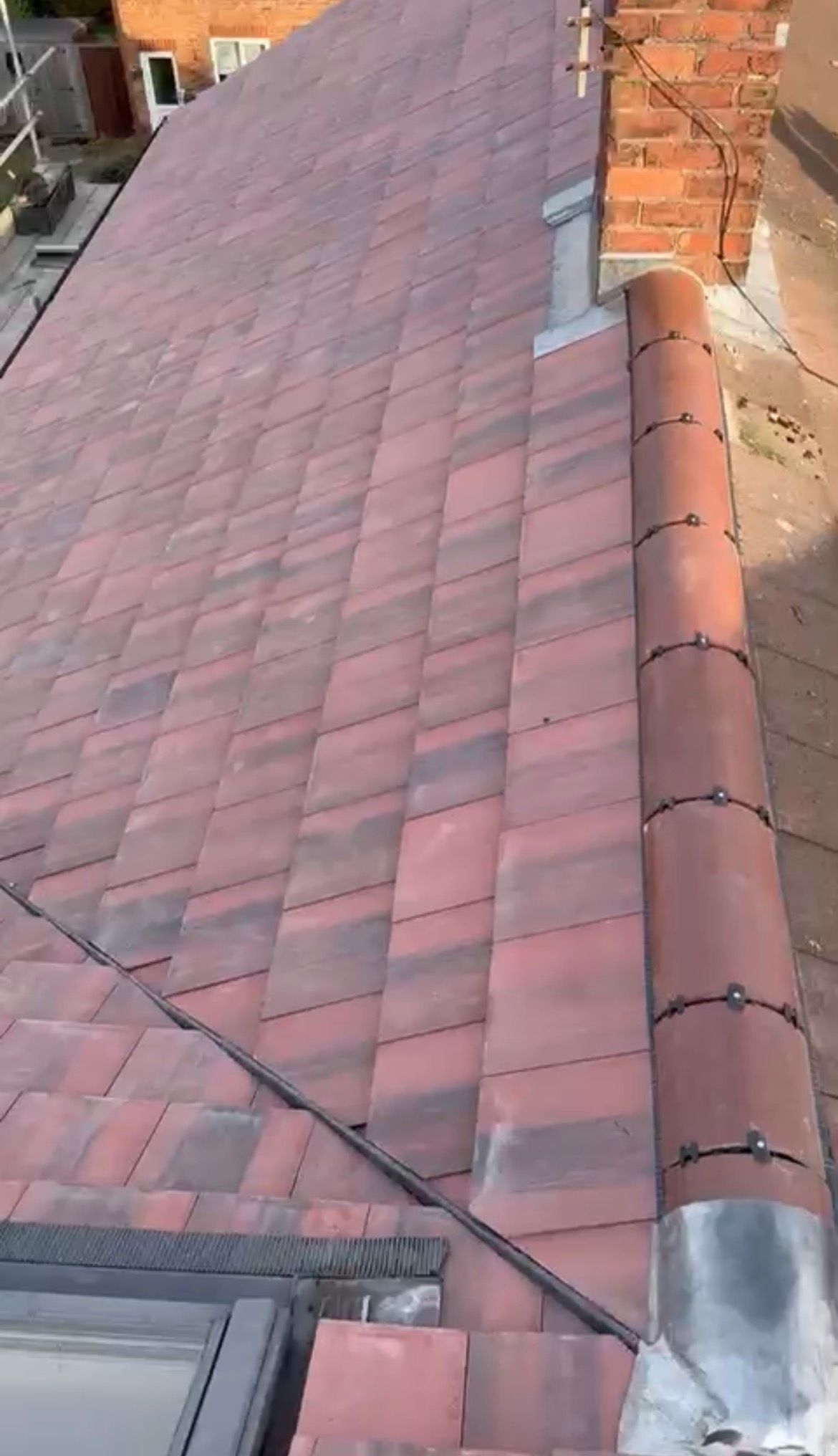 Red-tiled sloped roof with a metal flashing seam beside a brick wall and gutter