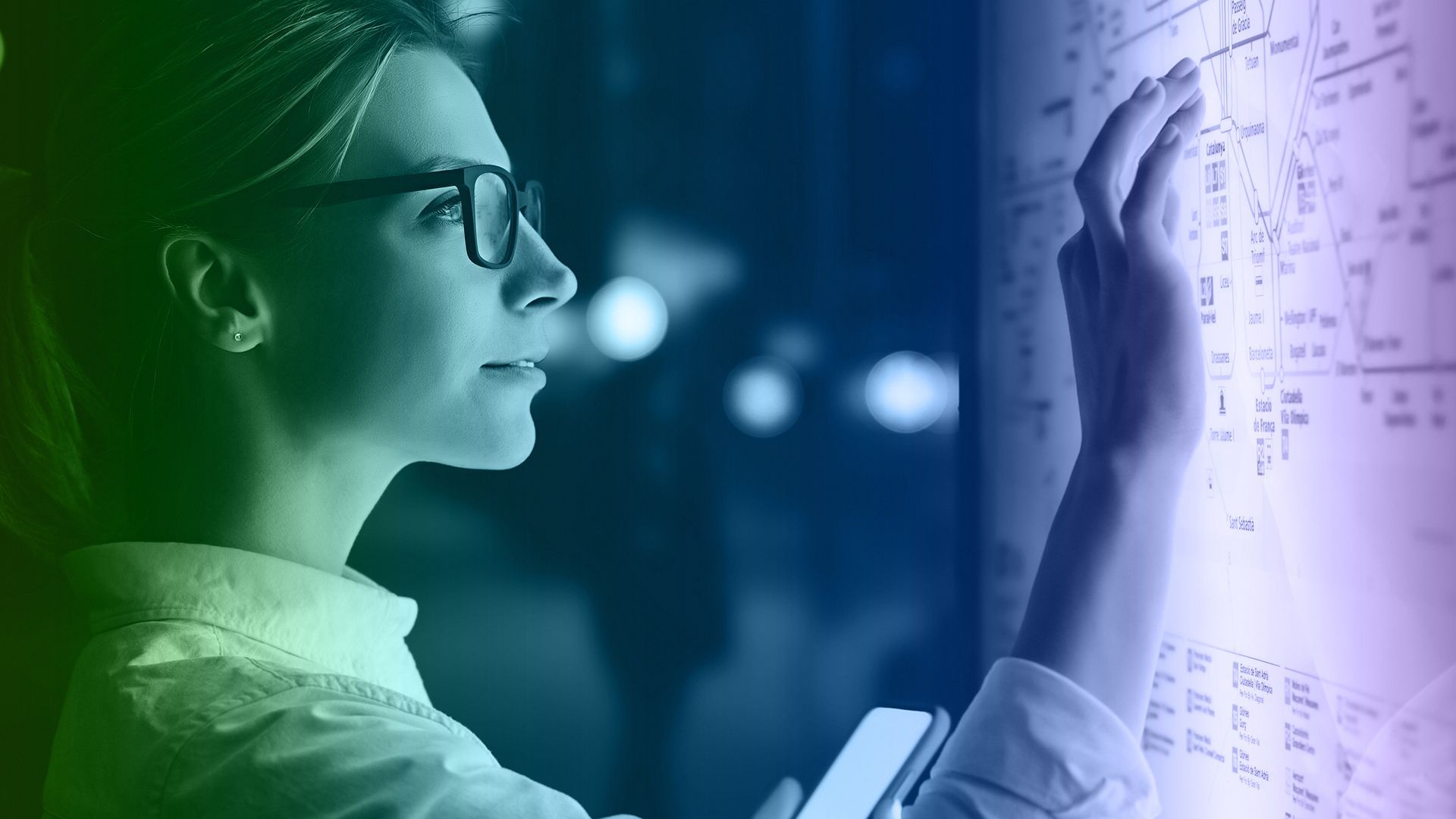 Woman in glasses looking at a glowing, touch-screen display, touching it with her hand.