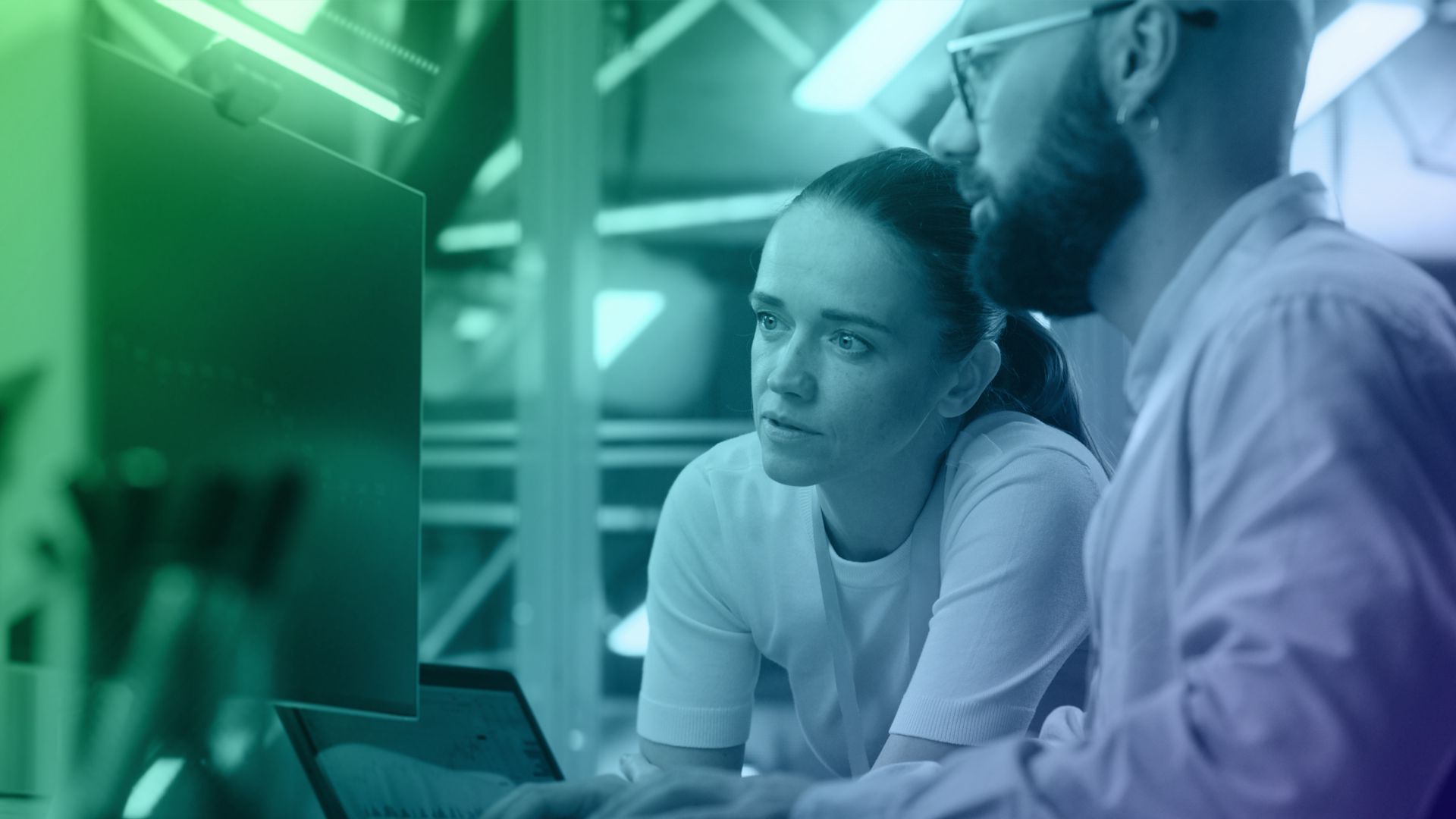 Two people in an office, focused on a monitor under green-blue lighting