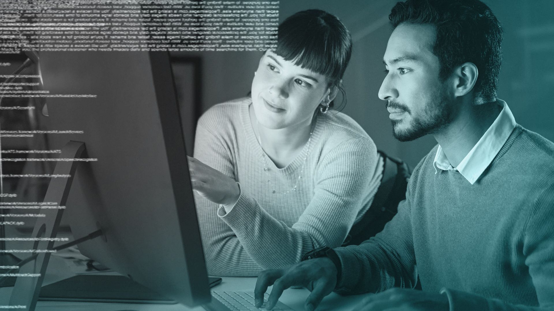 Two coworkers reviewing code on a computer screen in a blue-lit office