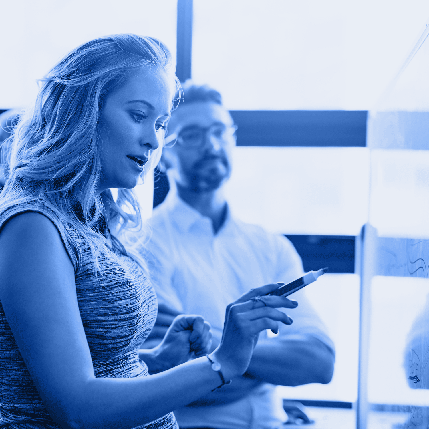 Woman pointing at whiteboard, explaining something to a man in office. Blue-toned.