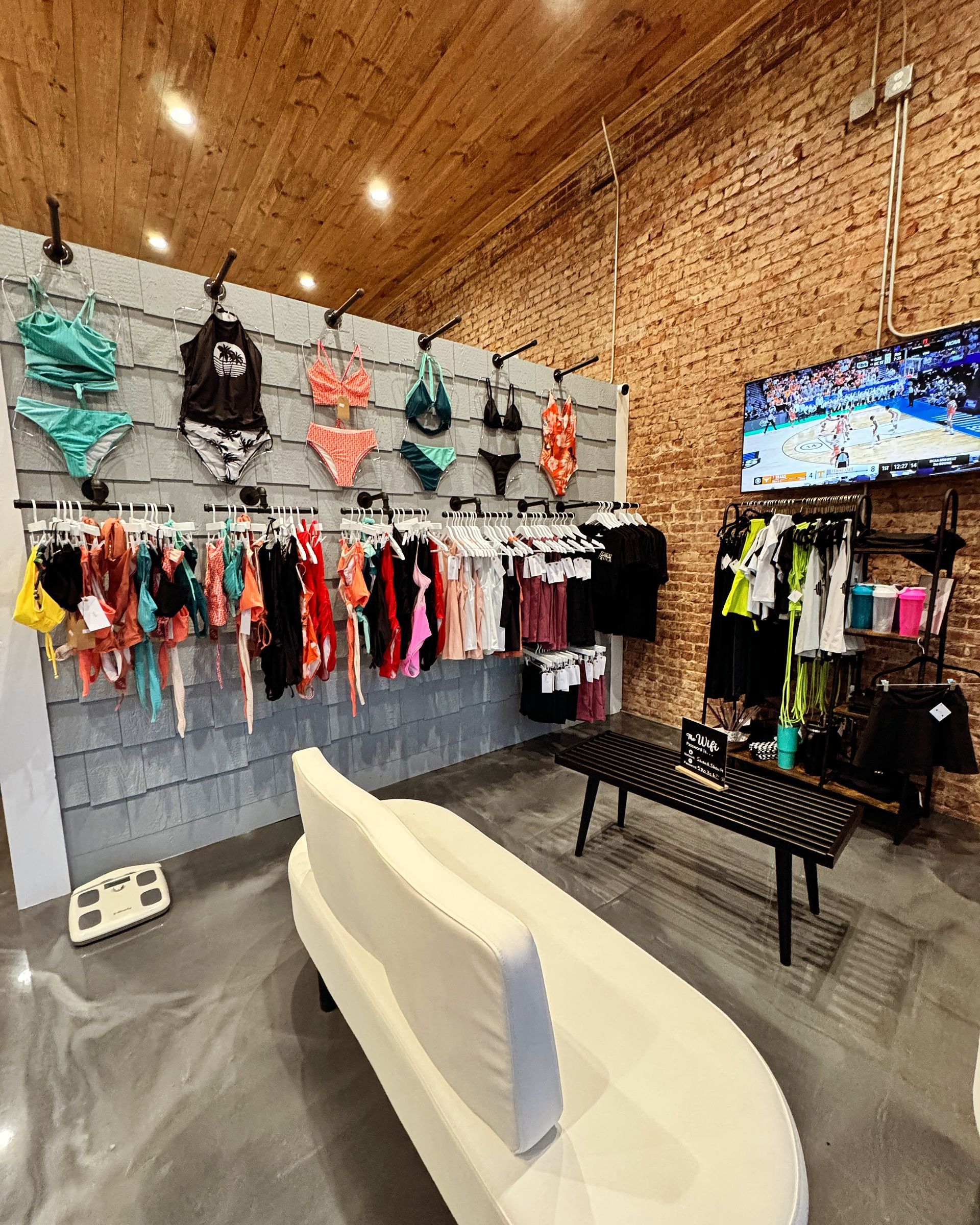 A room with a couch , table , and clothes hanging on a wall.