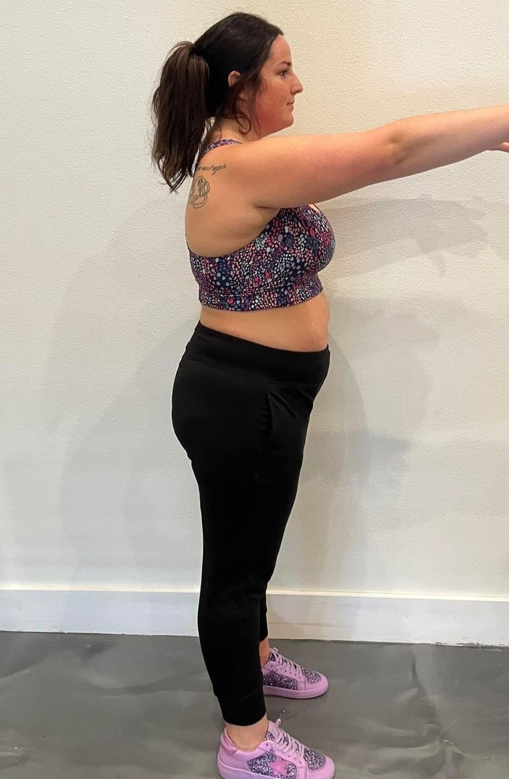 a woman in a crop top and black pants is standing in front of a wall .