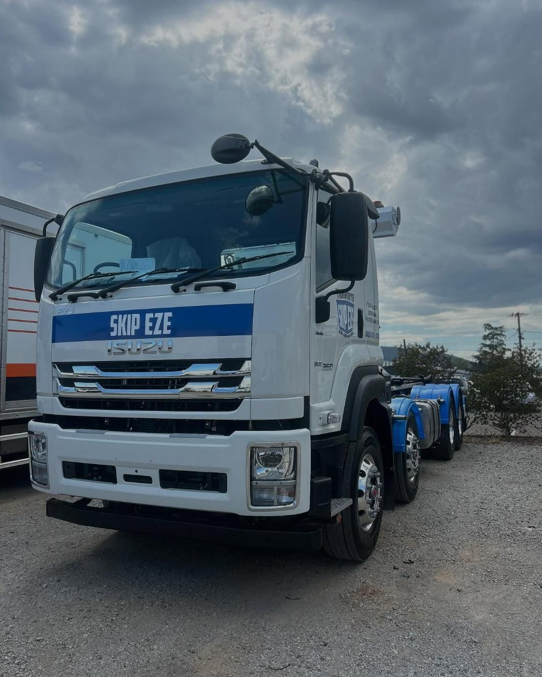 A White Truck With A Blue Stripe On The Front Is Parked In A Gravel Lot — Tamworth Skip Eze In Taminda, NSW