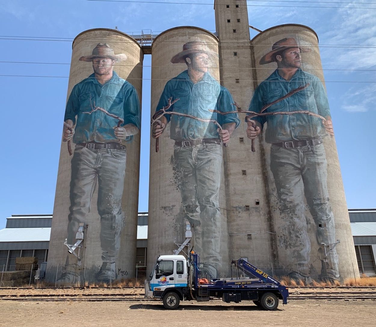 A Truck Is Parked In Front Of Three Silos With Cowboys Painted On Them — Tamworth Skip Eze In Taminda, NSW