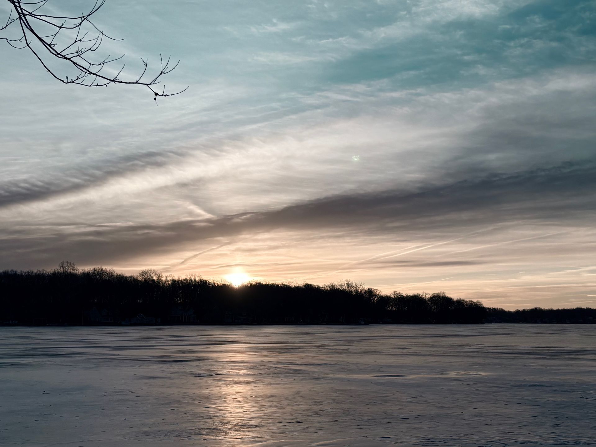Sunset over a frozen lake with silhouetted trees and streaked clouds