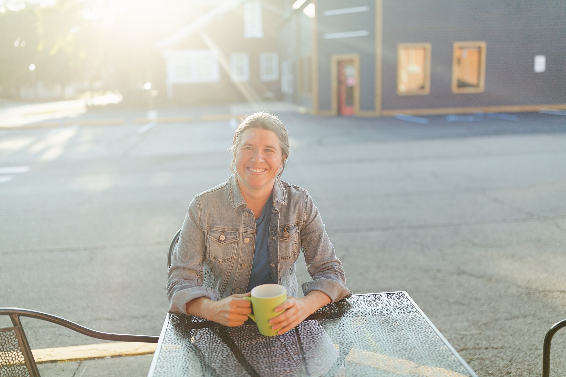 Person smiling at an outdoor café table, holding a cup in warm sunlight