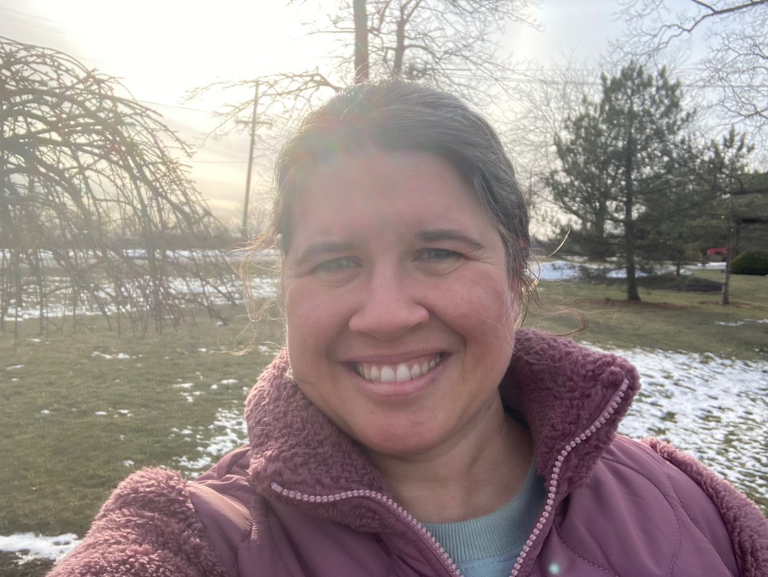 Smiling person outdoors in a pink jacket with snowy ground and trees in the background