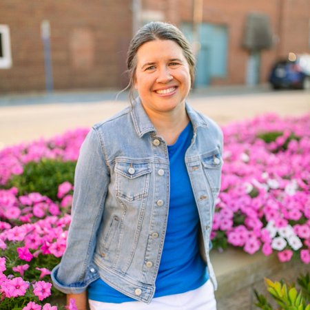 Smiling person in a denim jacket standing by bright pink flowers outdoors