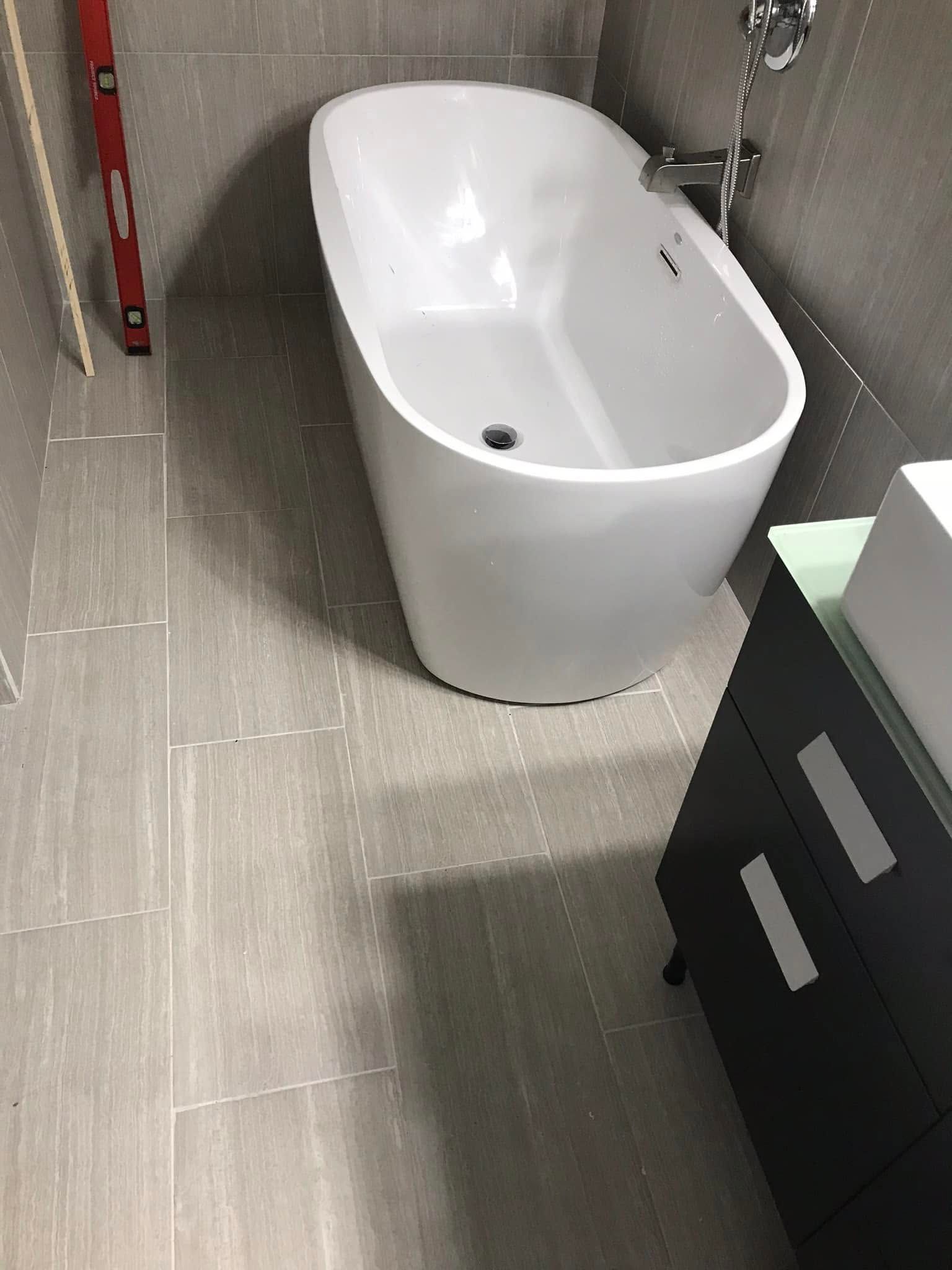 Small bathroom with a white freestanding tub on gray tile, beside a dark vanity and wall-mounted towel rack.