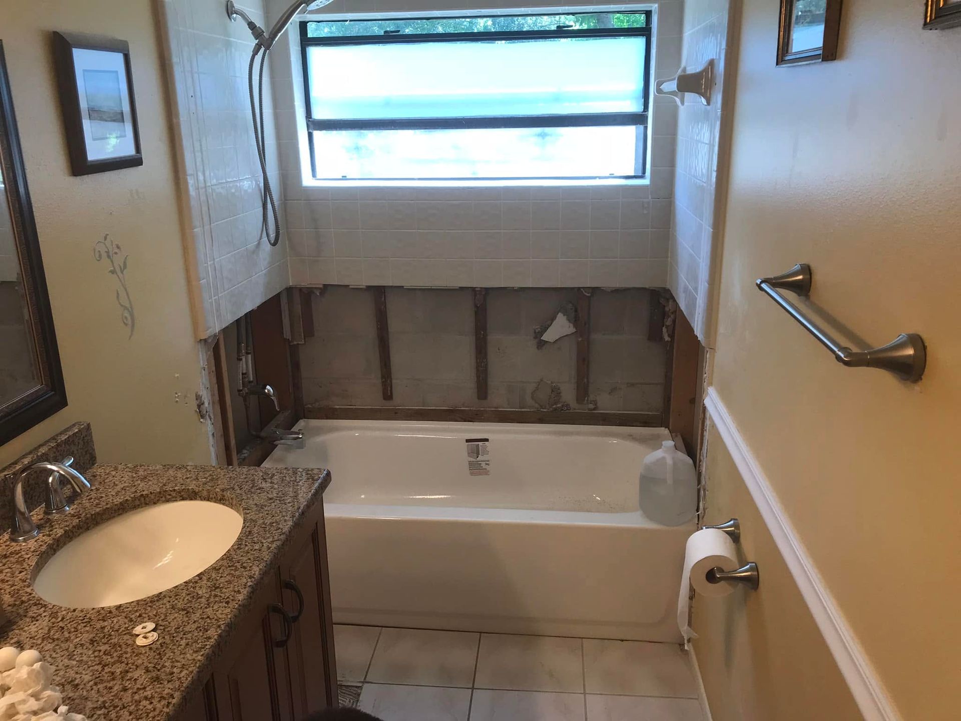 Small bathroom under renovation with exposed wall studs around a bathtub and a sink vanity.