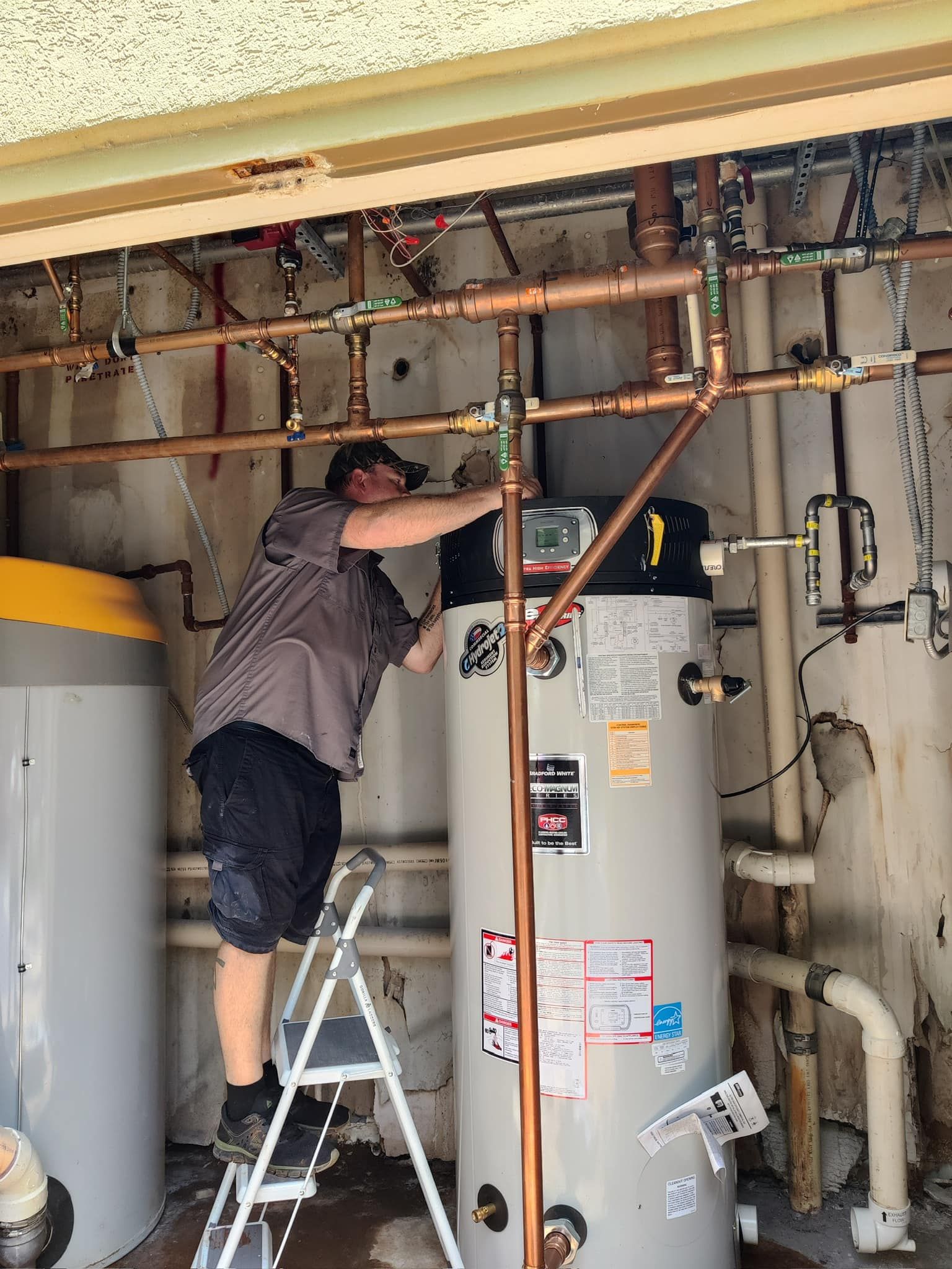 Person on a step stool working on pipes and a water heater in a utility room.
