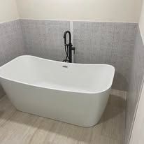 Modern freestanding white bathtub with black faucet against gray tiled bathroom wall