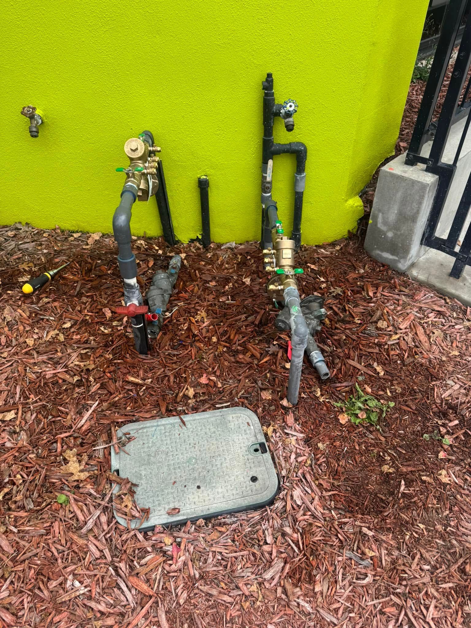Two toy guns propped against a lime-green wall over wood chips, with a concrete utility cover in front.