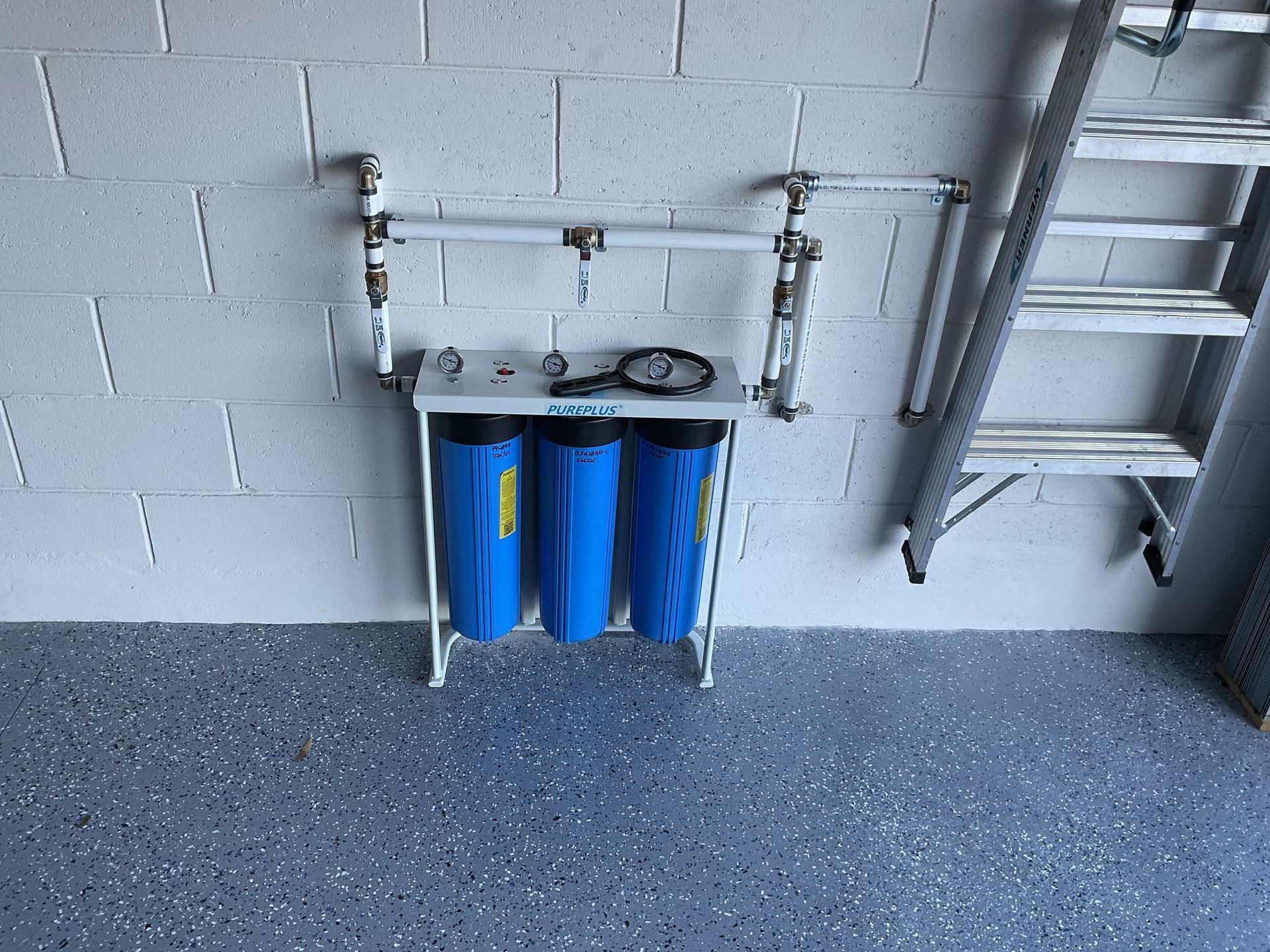 Wall-mounted utility sink with blue water filters in a garage or utility room.