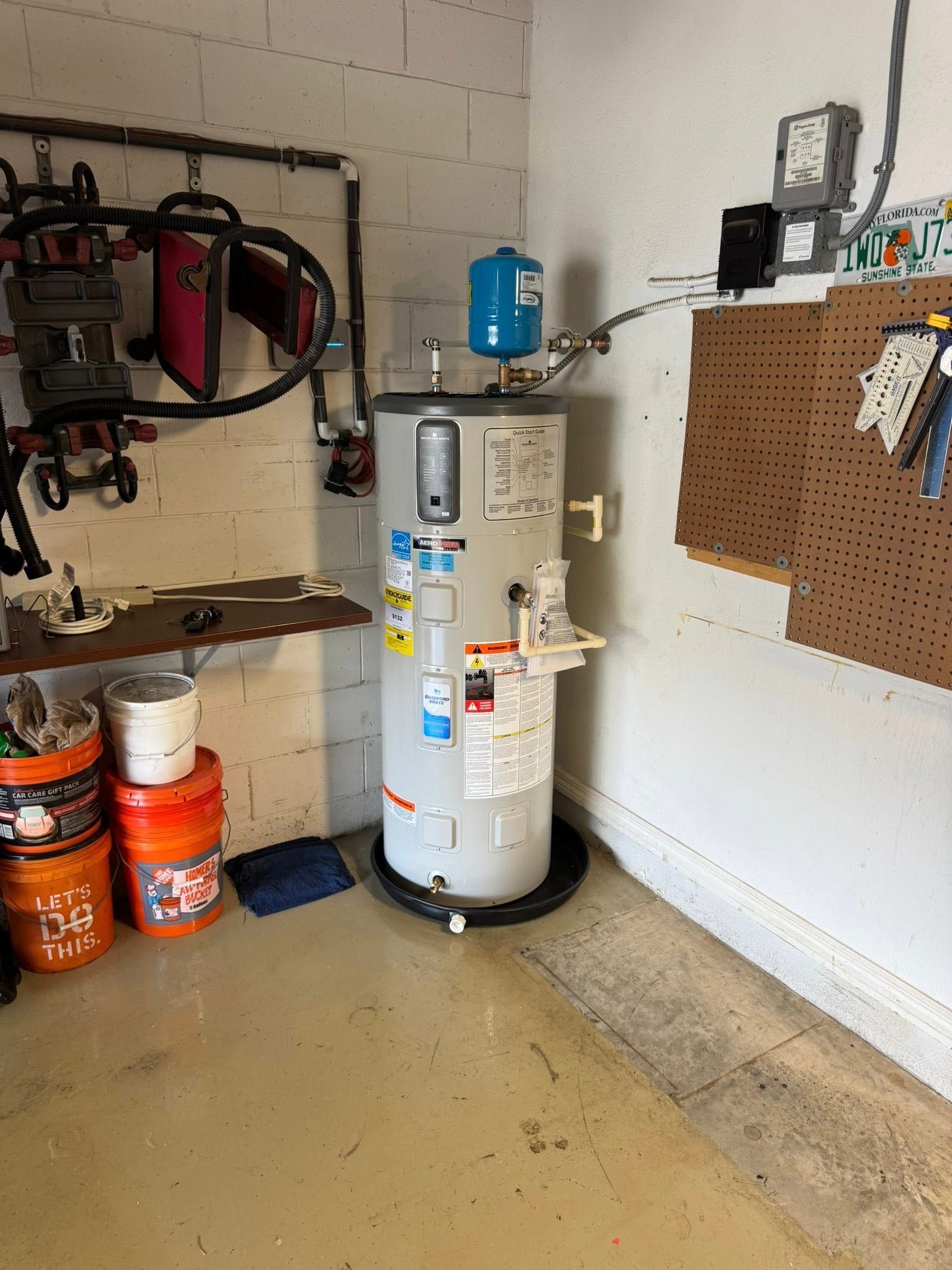 Garage utility room with a water heater, tools, and paint buckets on shelves and the floor