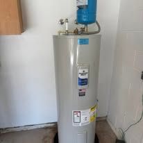 Tall beige water heater with blue tank on top, standing against a white wall in a utility room
