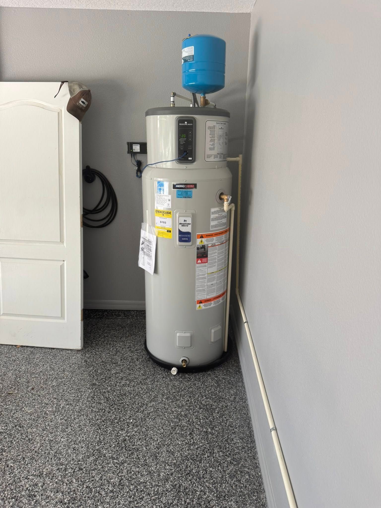 Water heater with blue expansion tank in a gray utility room corner.