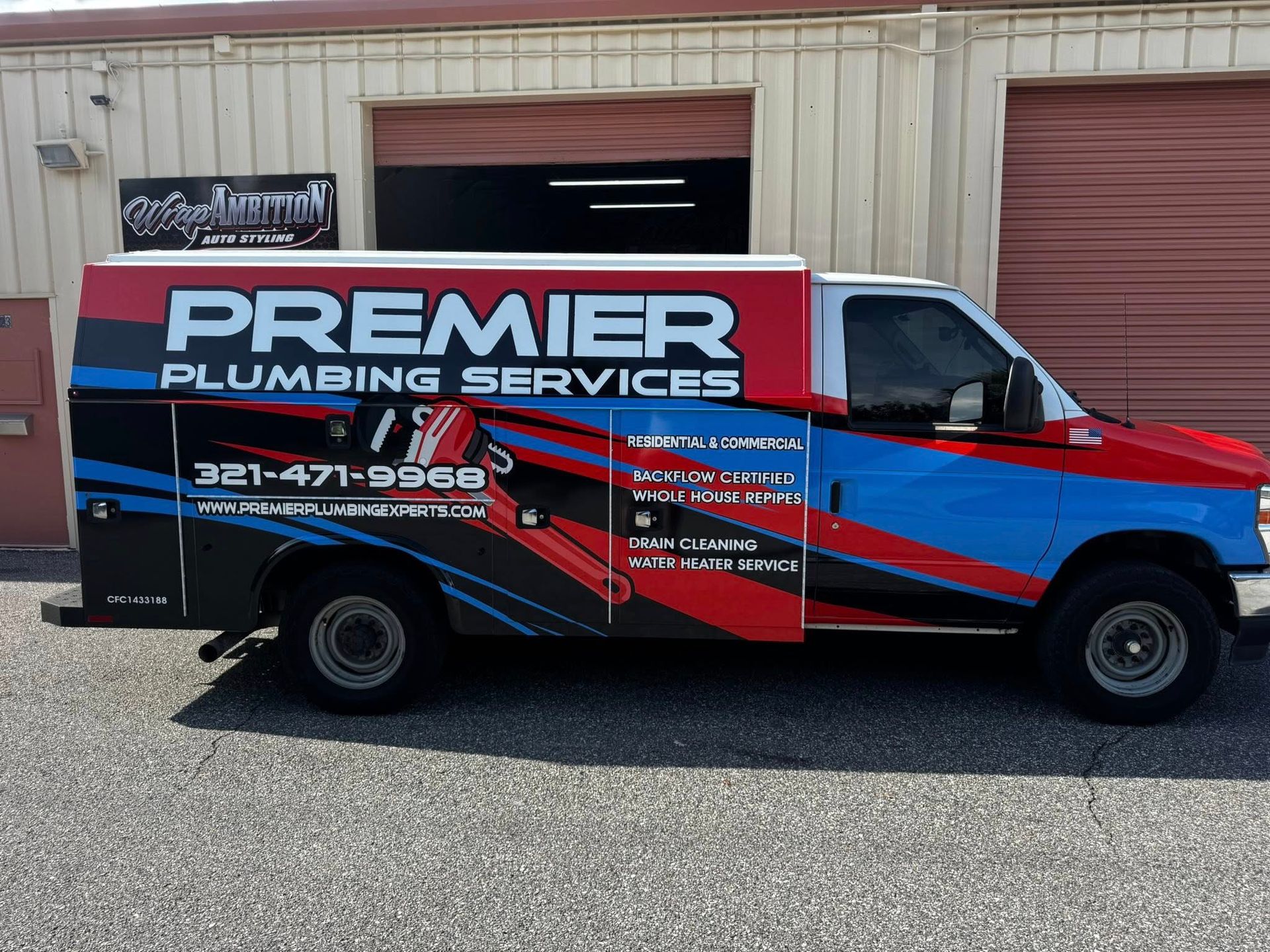 Red and black Premier Plumbing Services truck parked outside a metal building