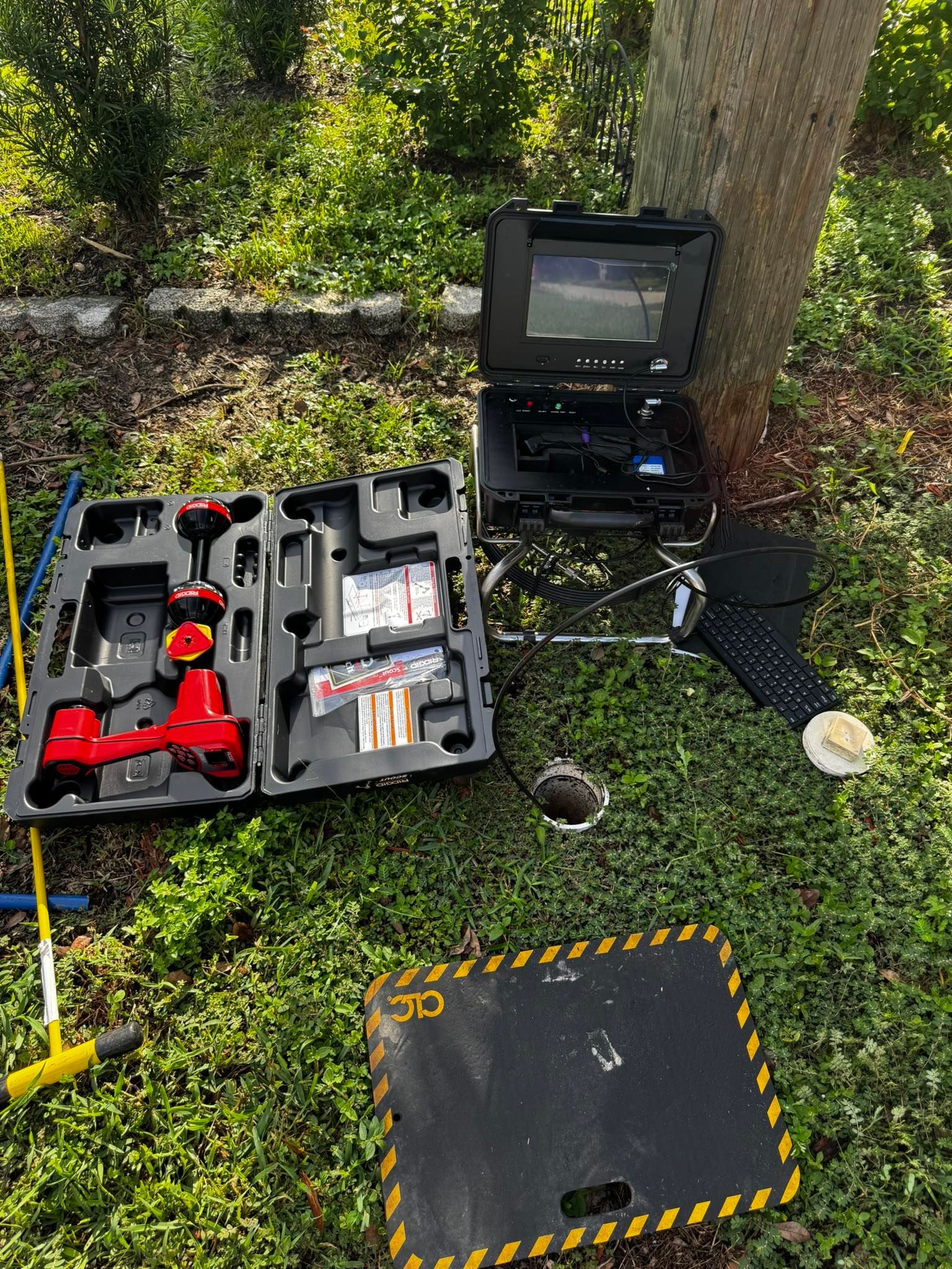 Tool kits and a yellow-marked ground panel beside a tree in a grassy outdoor area