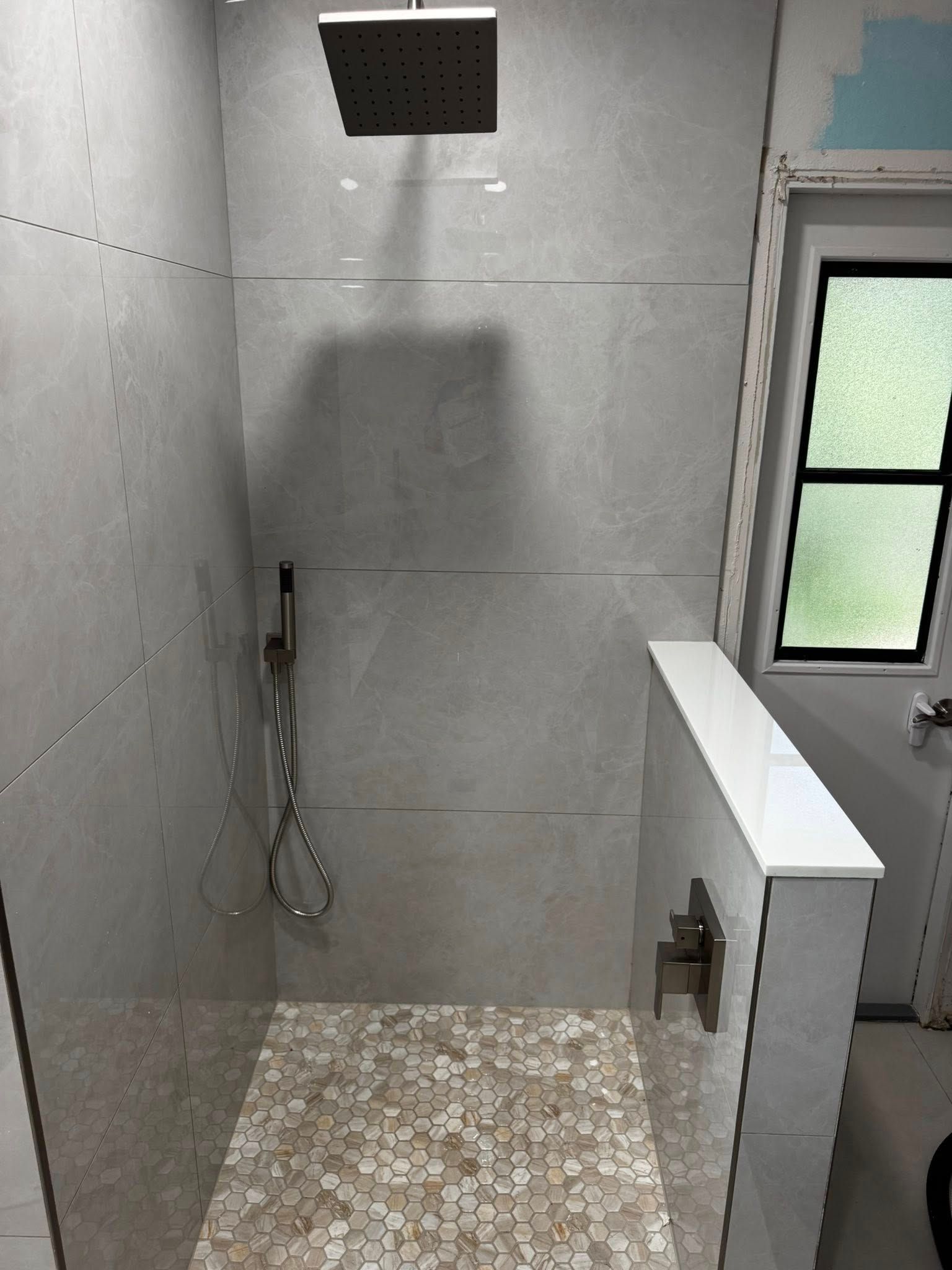 Modern shower stall with gray tiled walls, pebble floor, rain showerhead, and a frosted window.