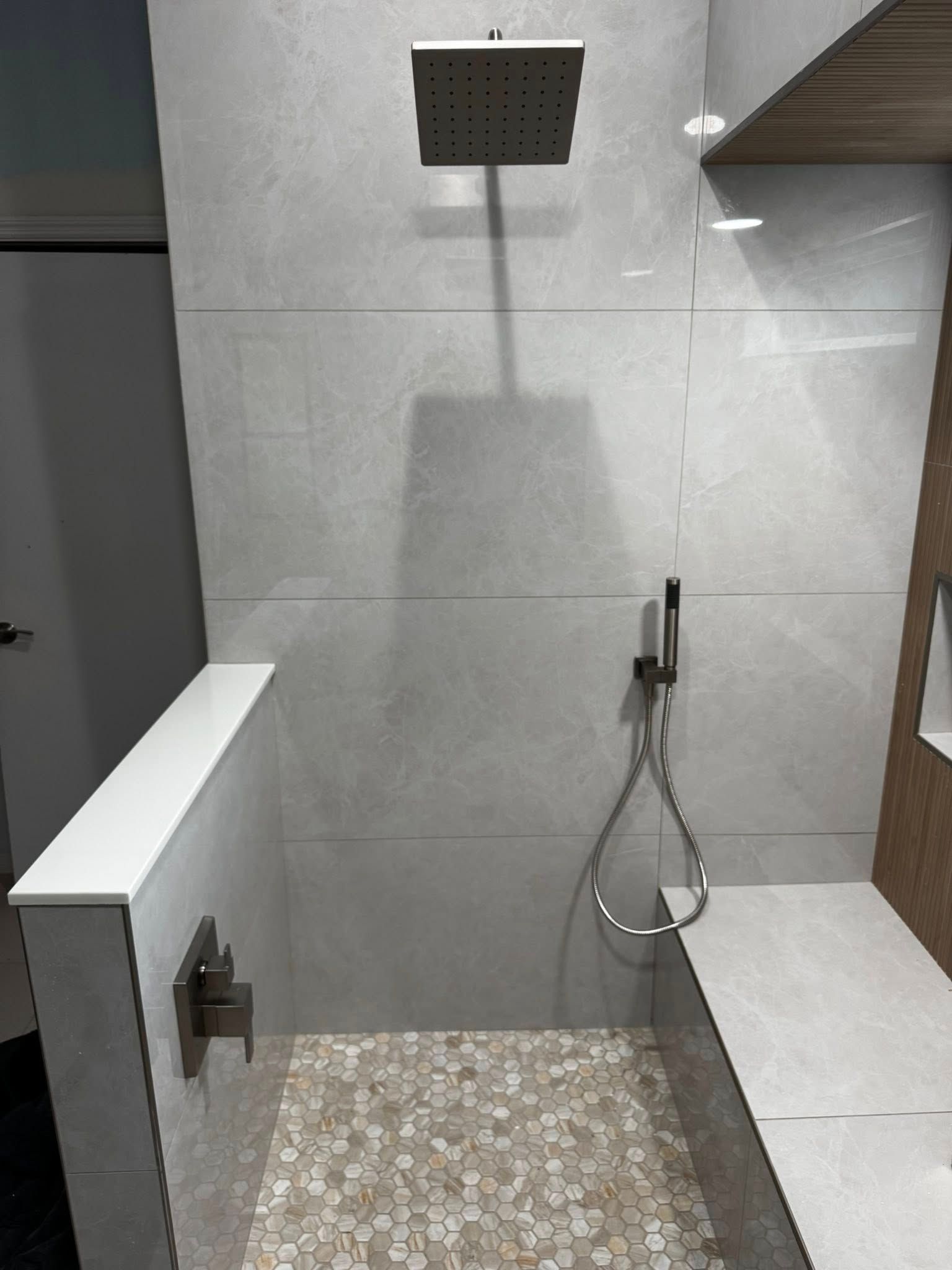 Modern bathroom with a wall-mounted shower, gray tile, and a pebble-textured floor area