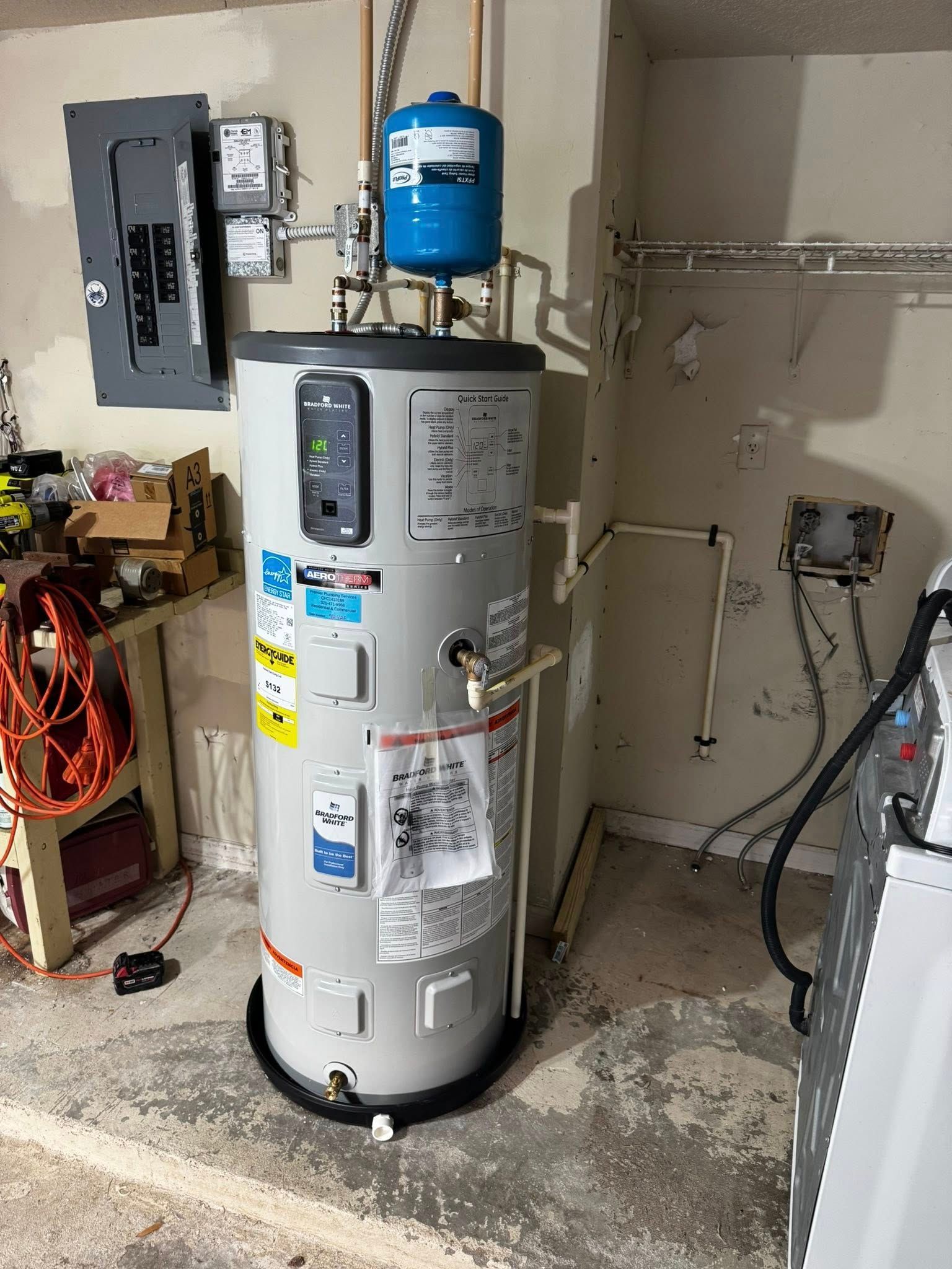 Water heater with blue expansion tank in a garage utility area next to electrical panel and wall wiring