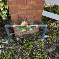 Outdoor gas meter with black pipes mounted on a brick wall, with a yellow valve handle.