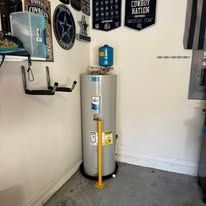 Water heater in a garage corner with a yellow pole protector and wall-mounted signs nearby