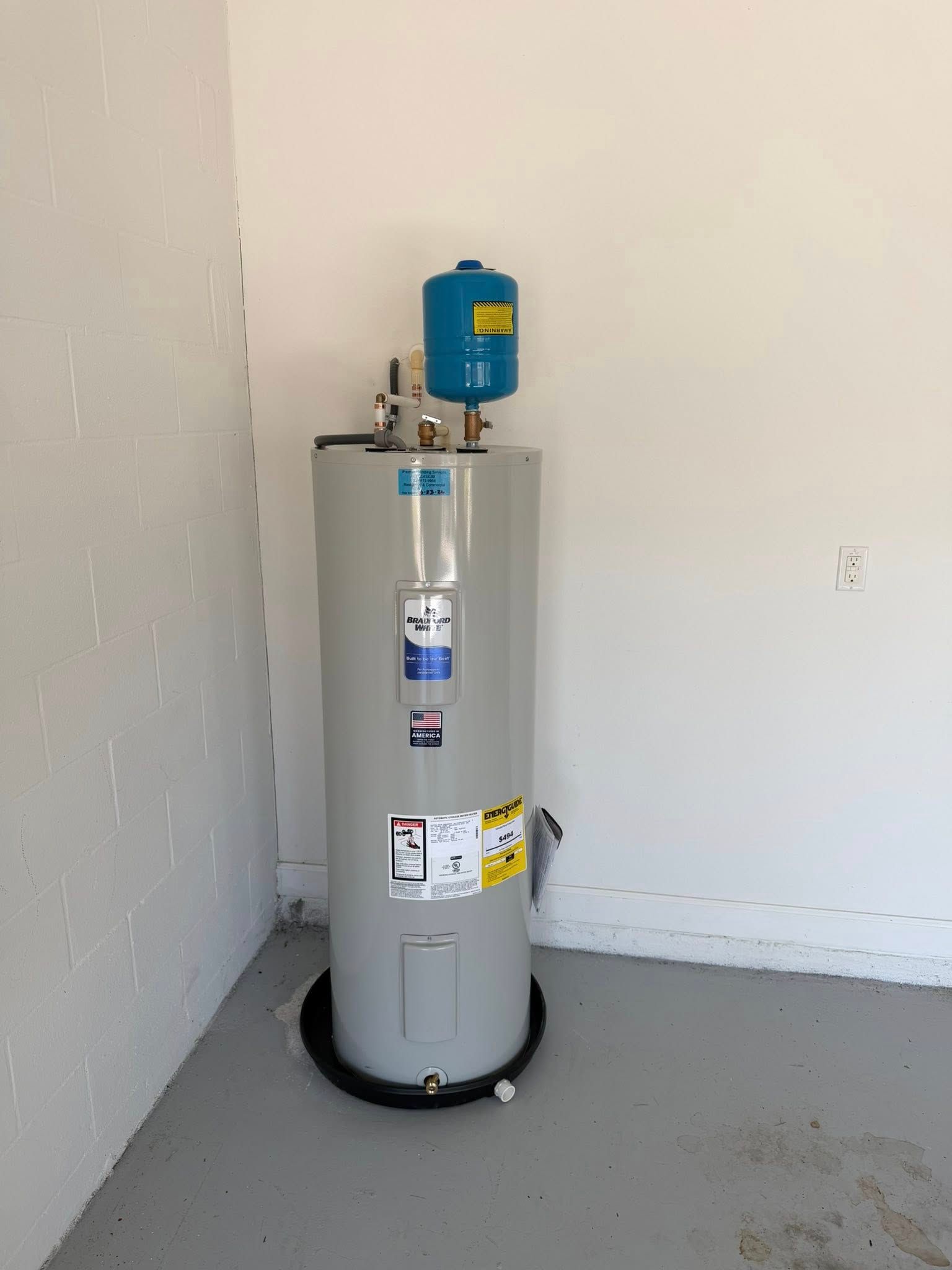 Water heater in a sparse corner of a room, with a blue expansion tank on top.