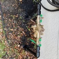 Outdoor brass irrigation valve assembly with green shutoff levers beside a white wall