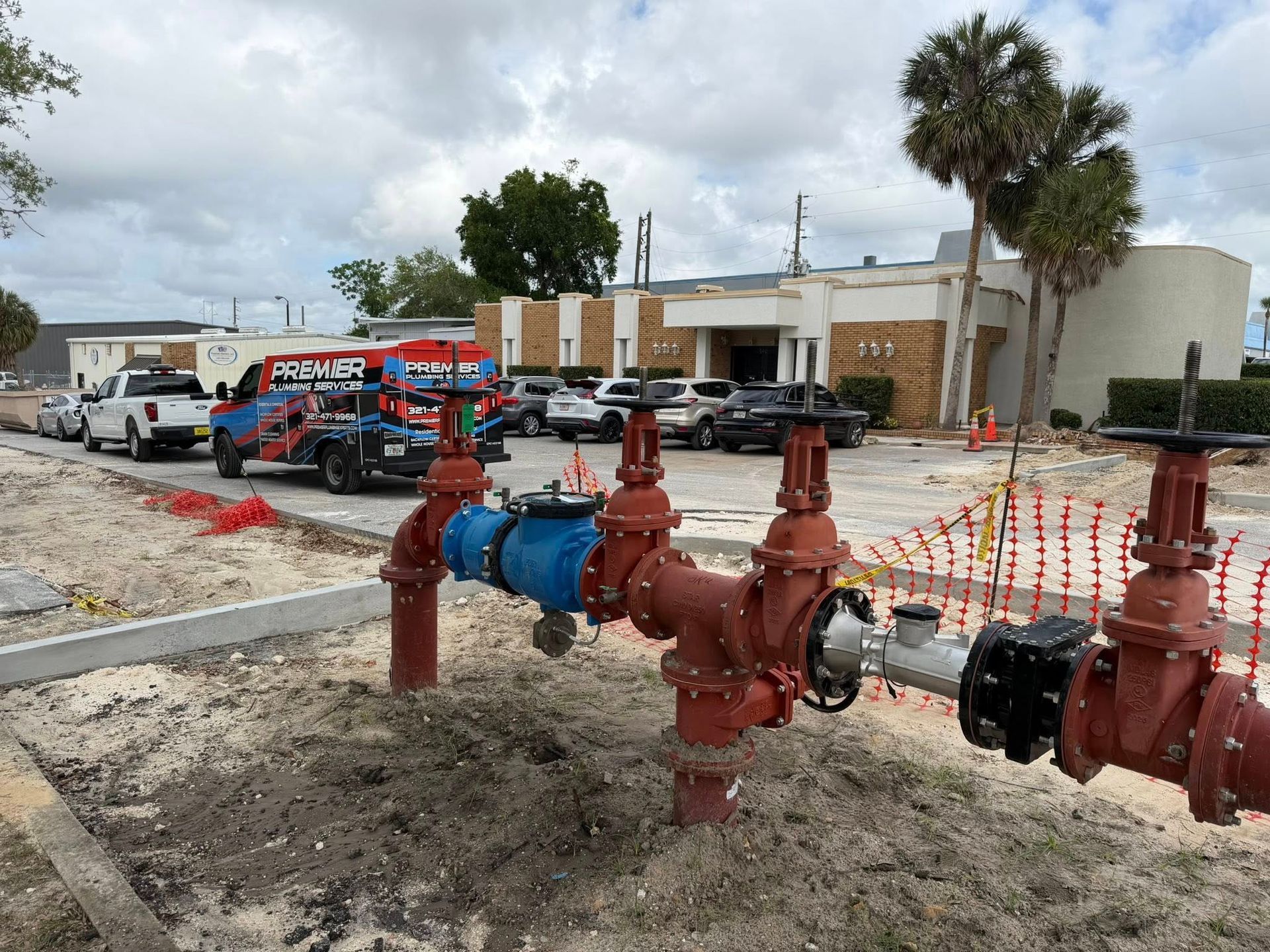 Red fire hydrant and blue pipeline in a sandy lot outside a low building with parked cars.