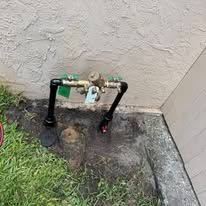 Outdoor gas line and shutoff valves beside a stucco wall, near grass and concrete.