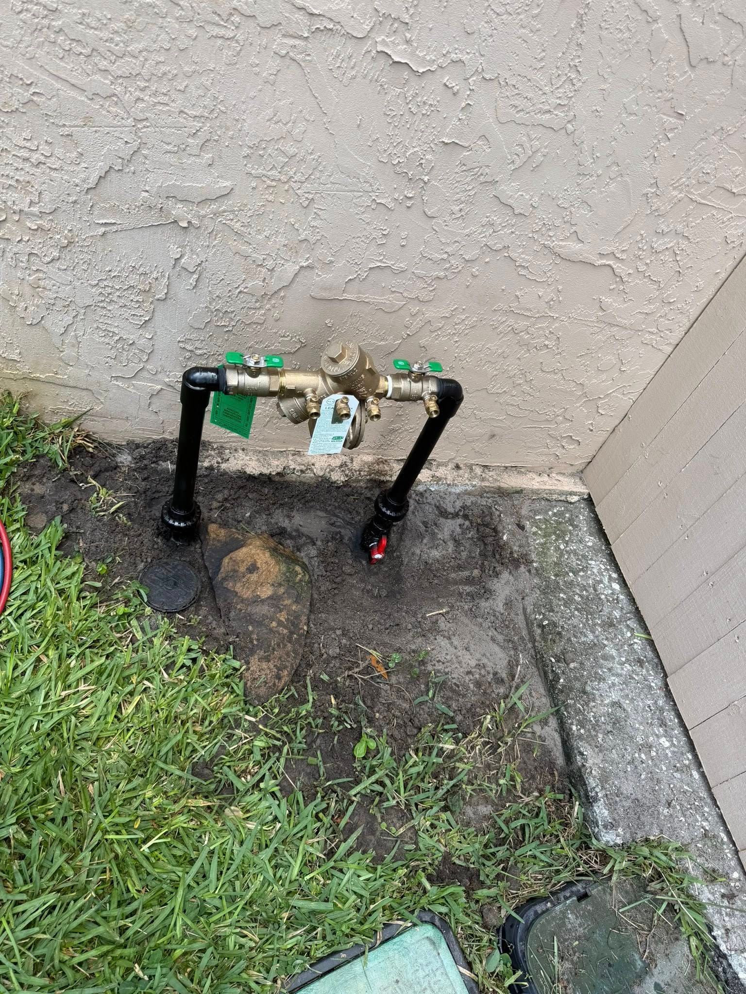 Outdoor gas meter and pipes mounted against a stucco wall beside grass and a concrete walkway.