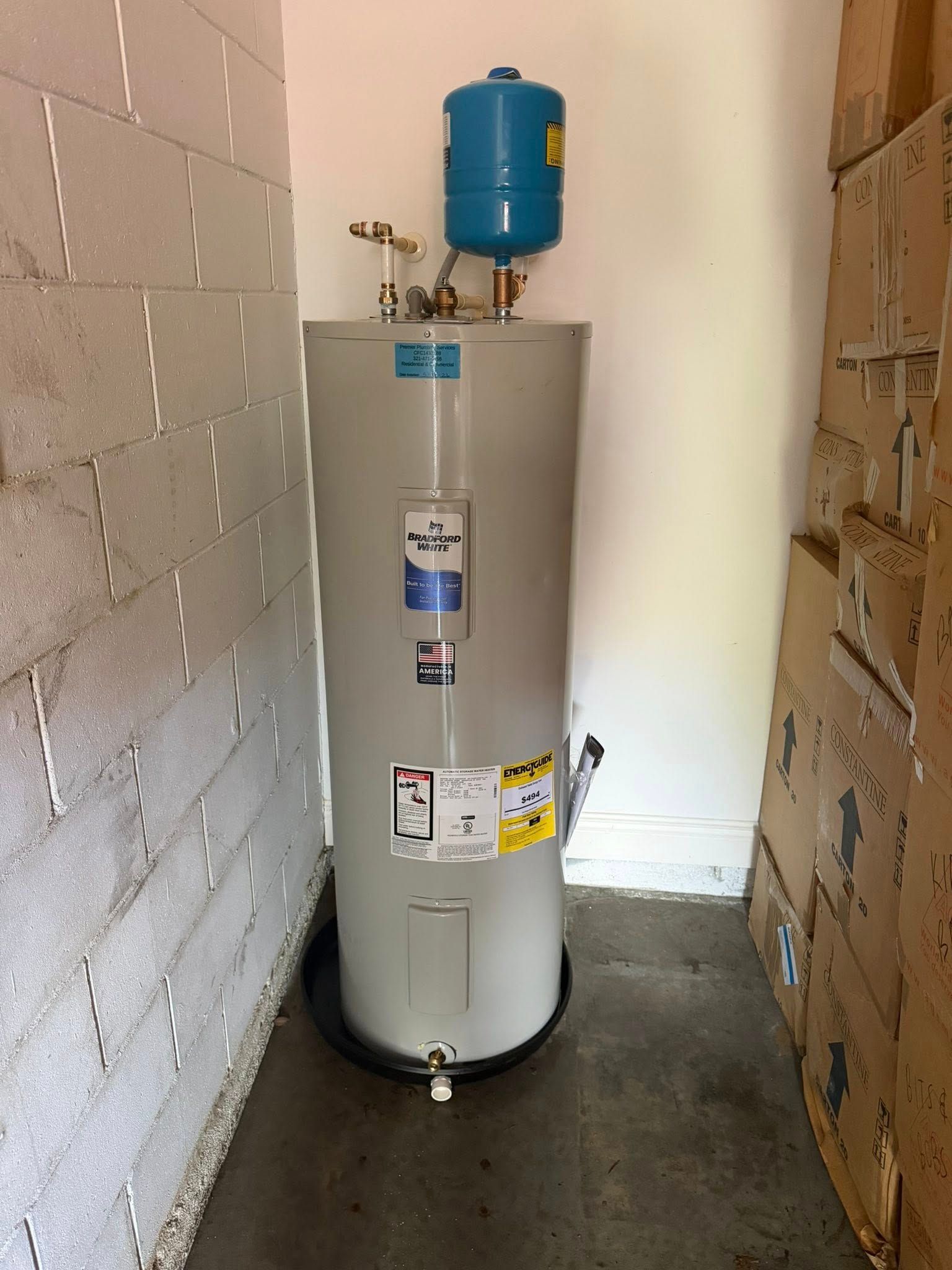Water heater with blue expansion tank in a narrow utility closet, flanked by unfinished walls.