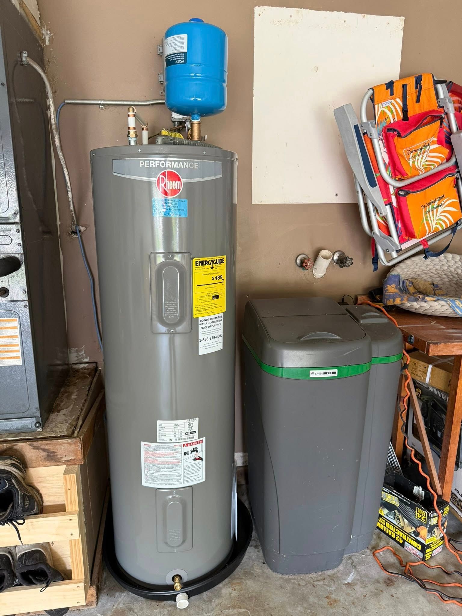 Water heater and gray utility tank in a basement, with storage items and tools nearby.