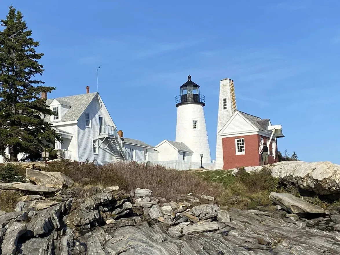 A lighthouse is sitting on top of a rocky hill next to a house.