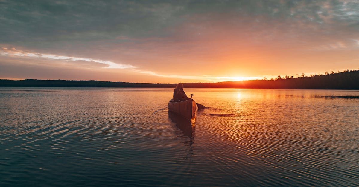 A person is paddling a kayak on a lake at sunset.