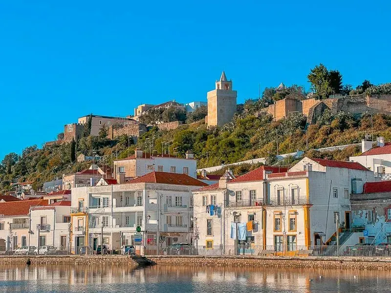 Coastal town with white buildings and a hilltop castle under a bright blue sky