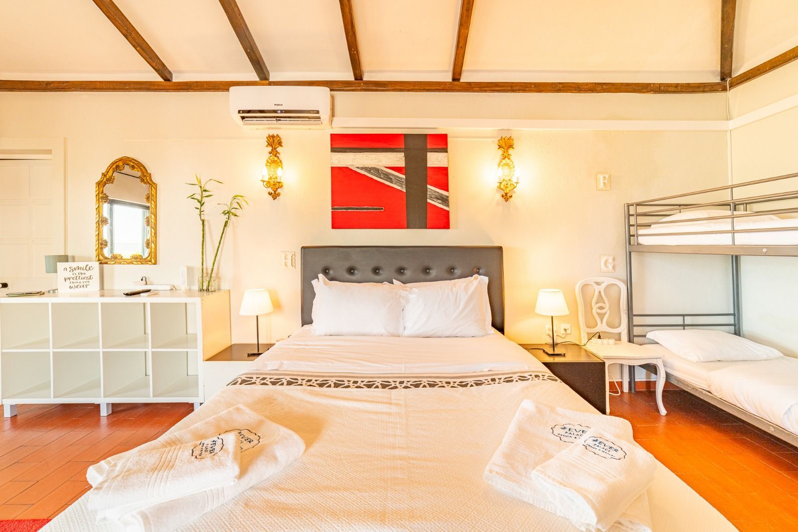 Bright tropical bedroom with a king bed, white bedding, red wall art, and bunk beds on the right