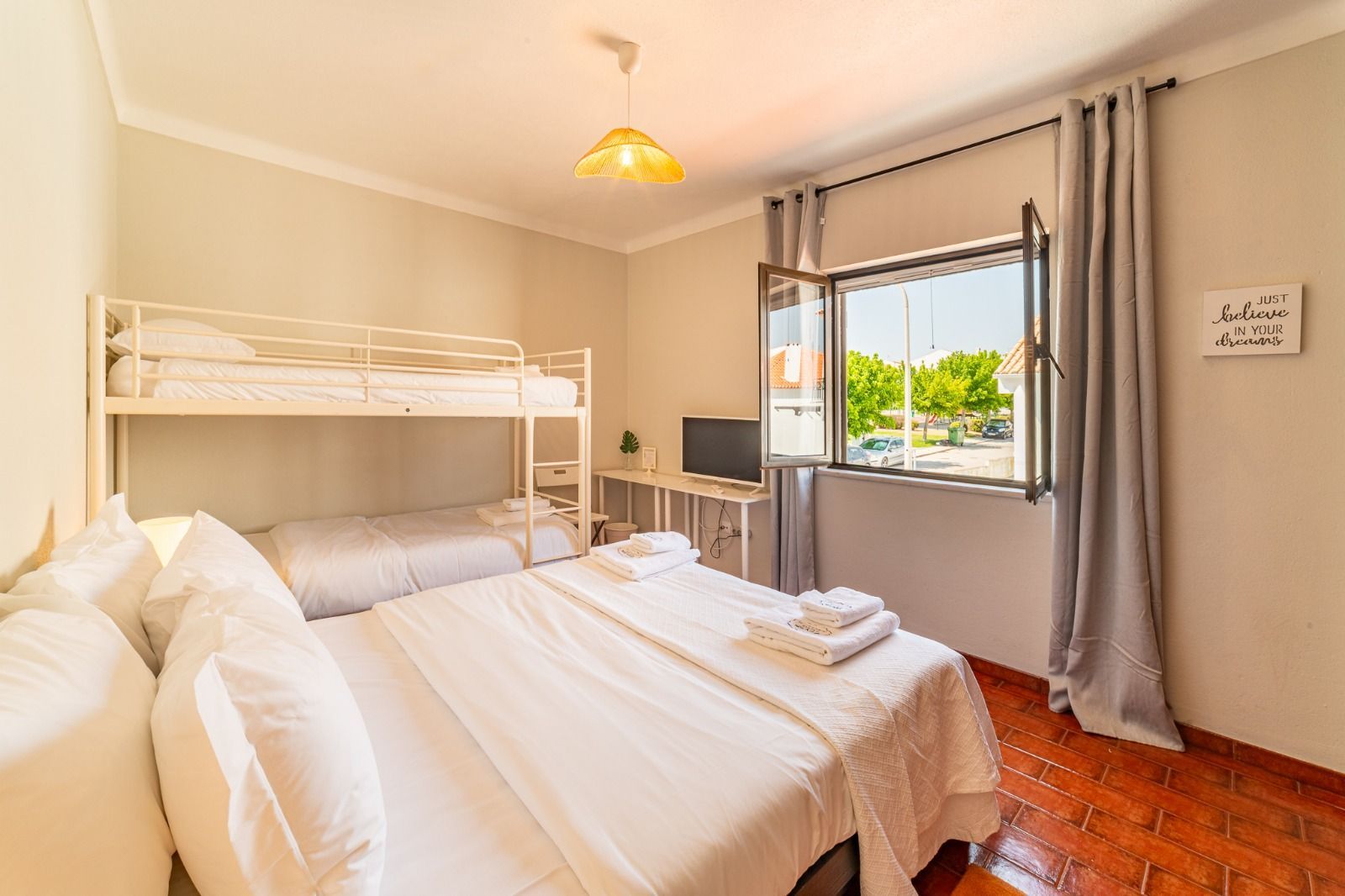 Bright bedroom with bunk bed, white bed, window, and wood floor