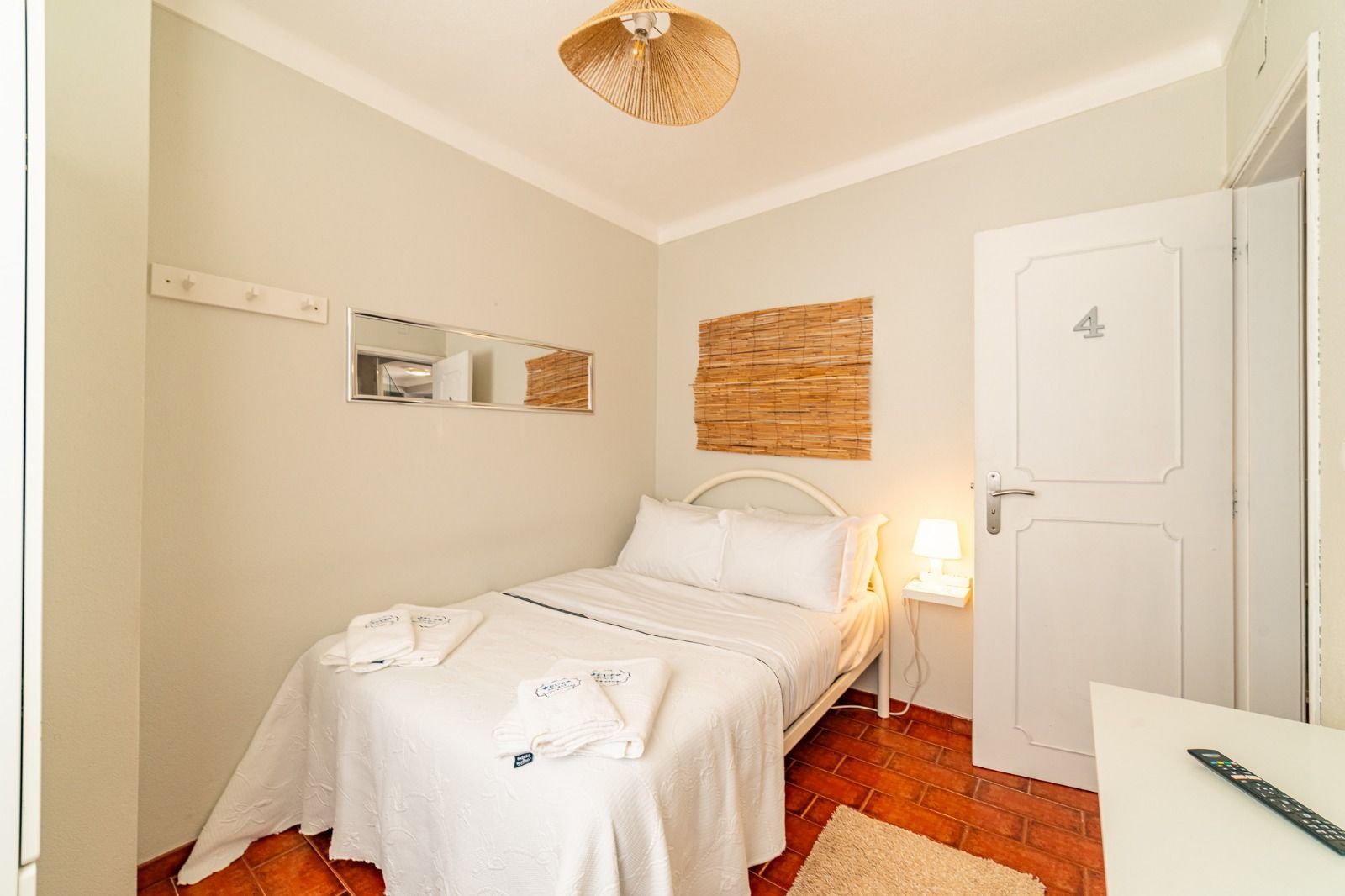 Small beige bedroom with a white bed, wicker wall decor, and a closed door
