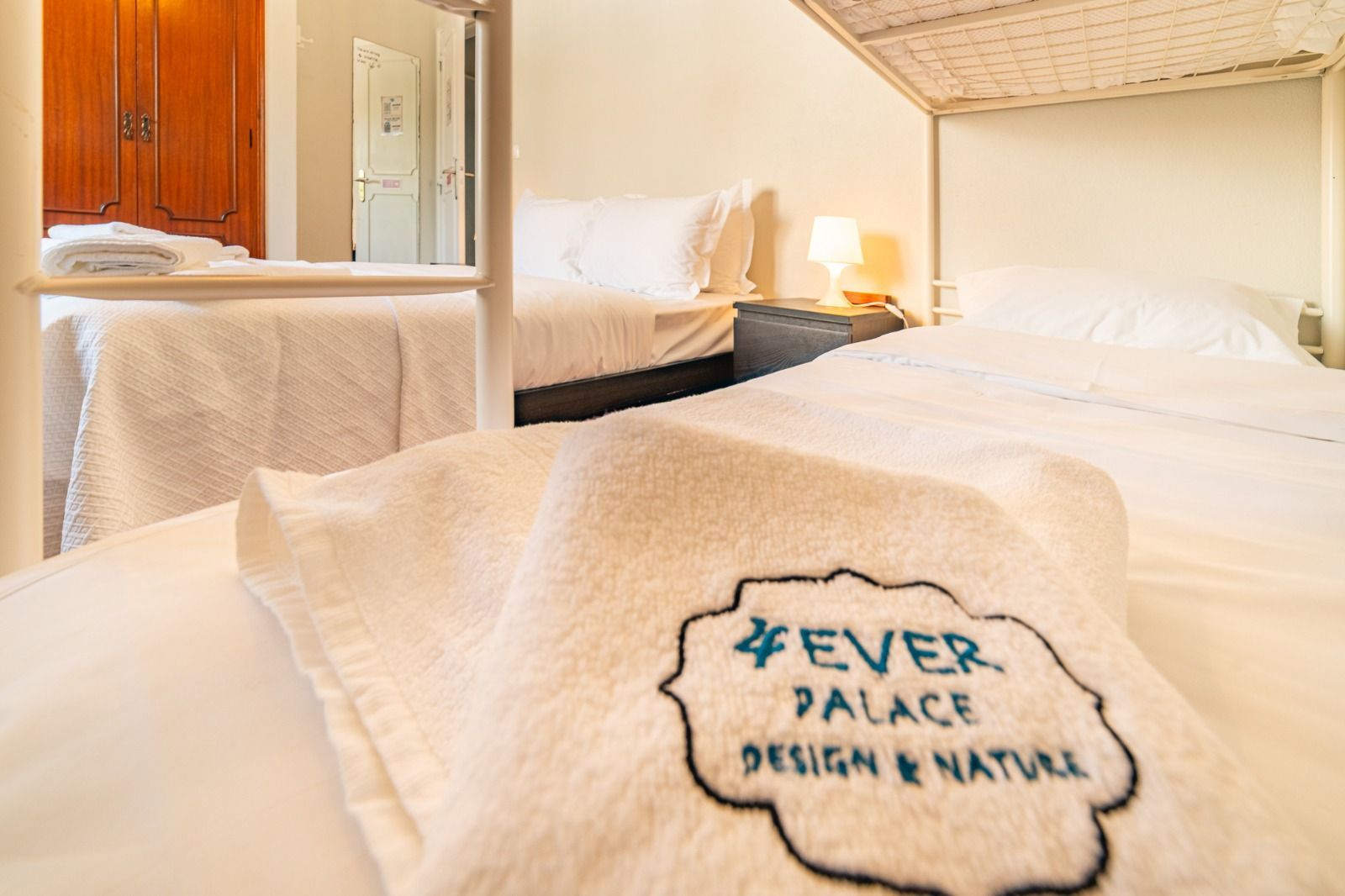Hotel room with neatly made bed and folded towel labeled “Ever Palace Design & Nature”