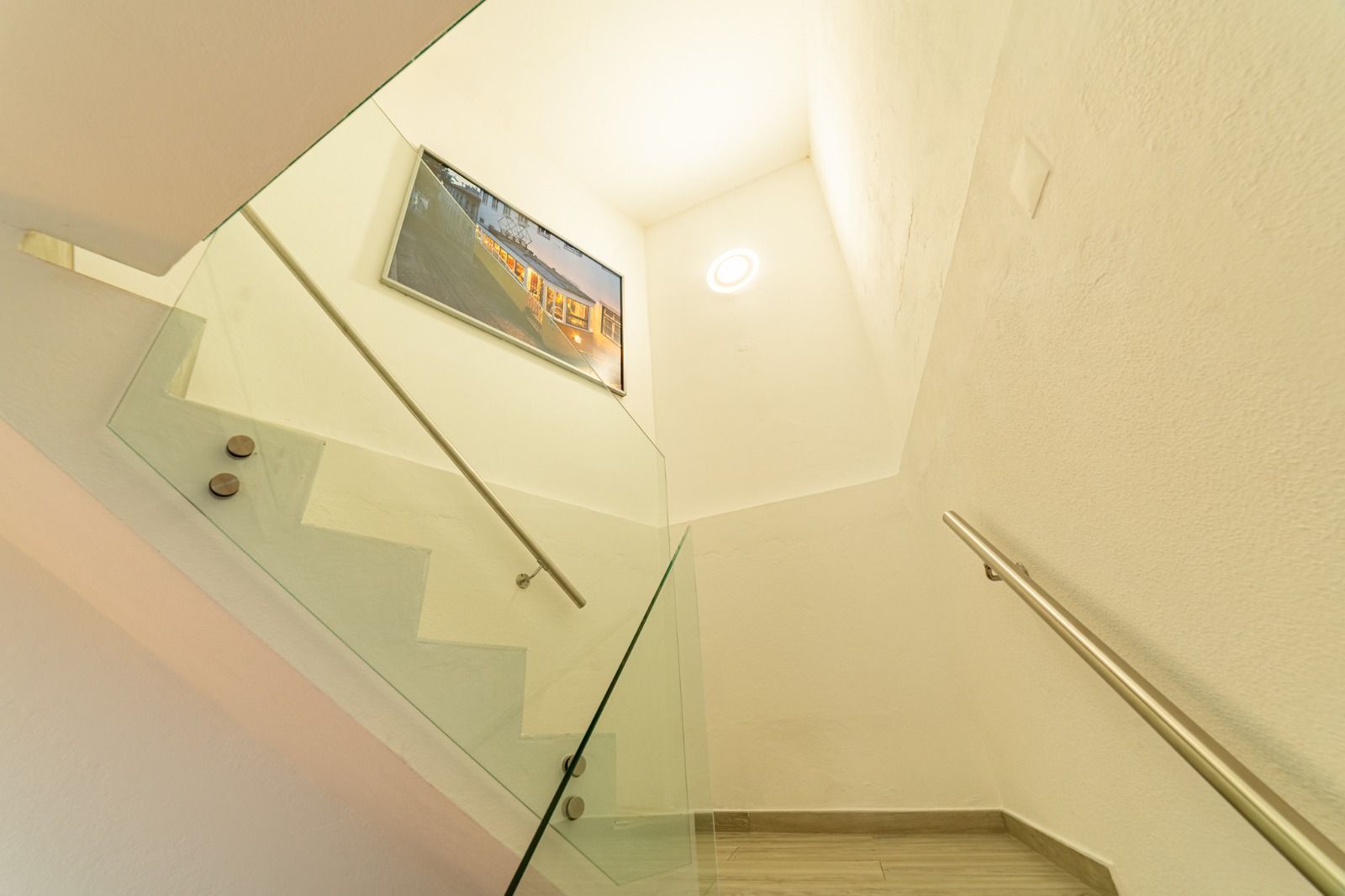 Stairwell with beige walls, glass railing, and a framed picture near the top landing.