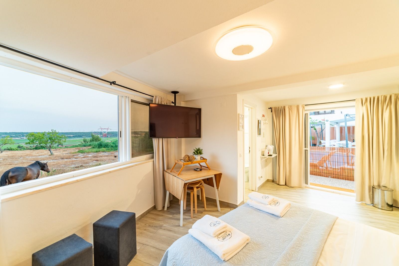 Bright seaside bedroom with twin beds, large window, desk, and balcony view of the ocean