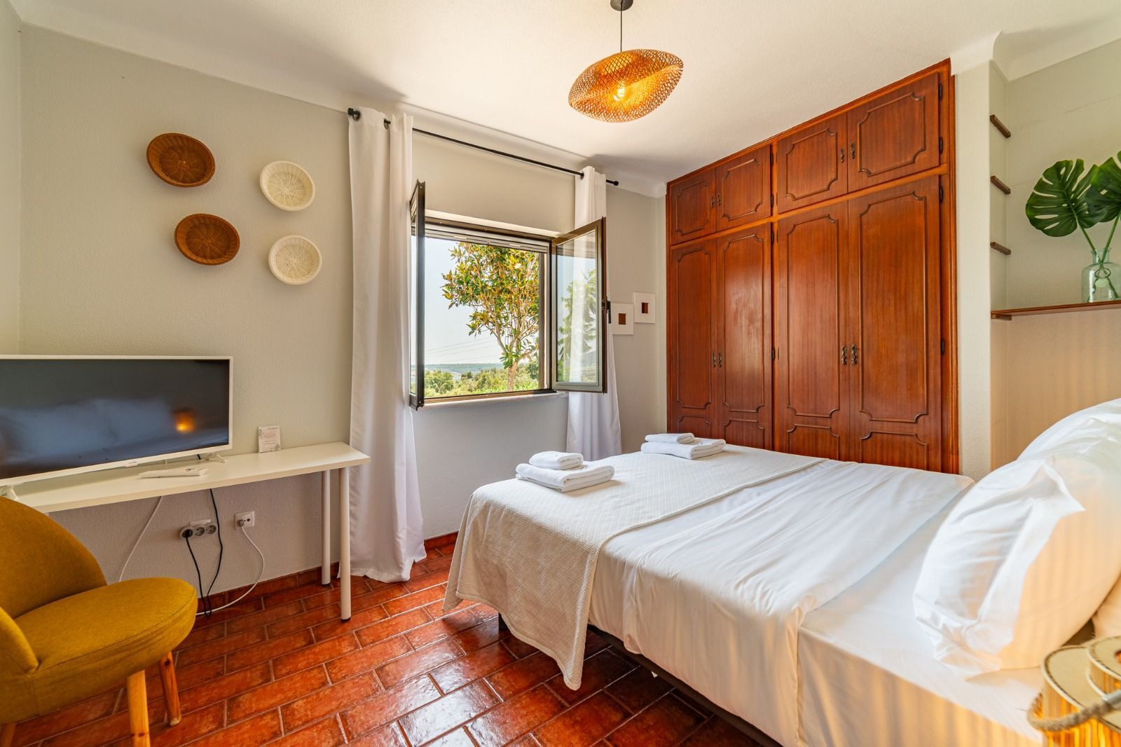 Bright bedroom with white bed, wooden wardrobe, desk, mustard chair, and open window