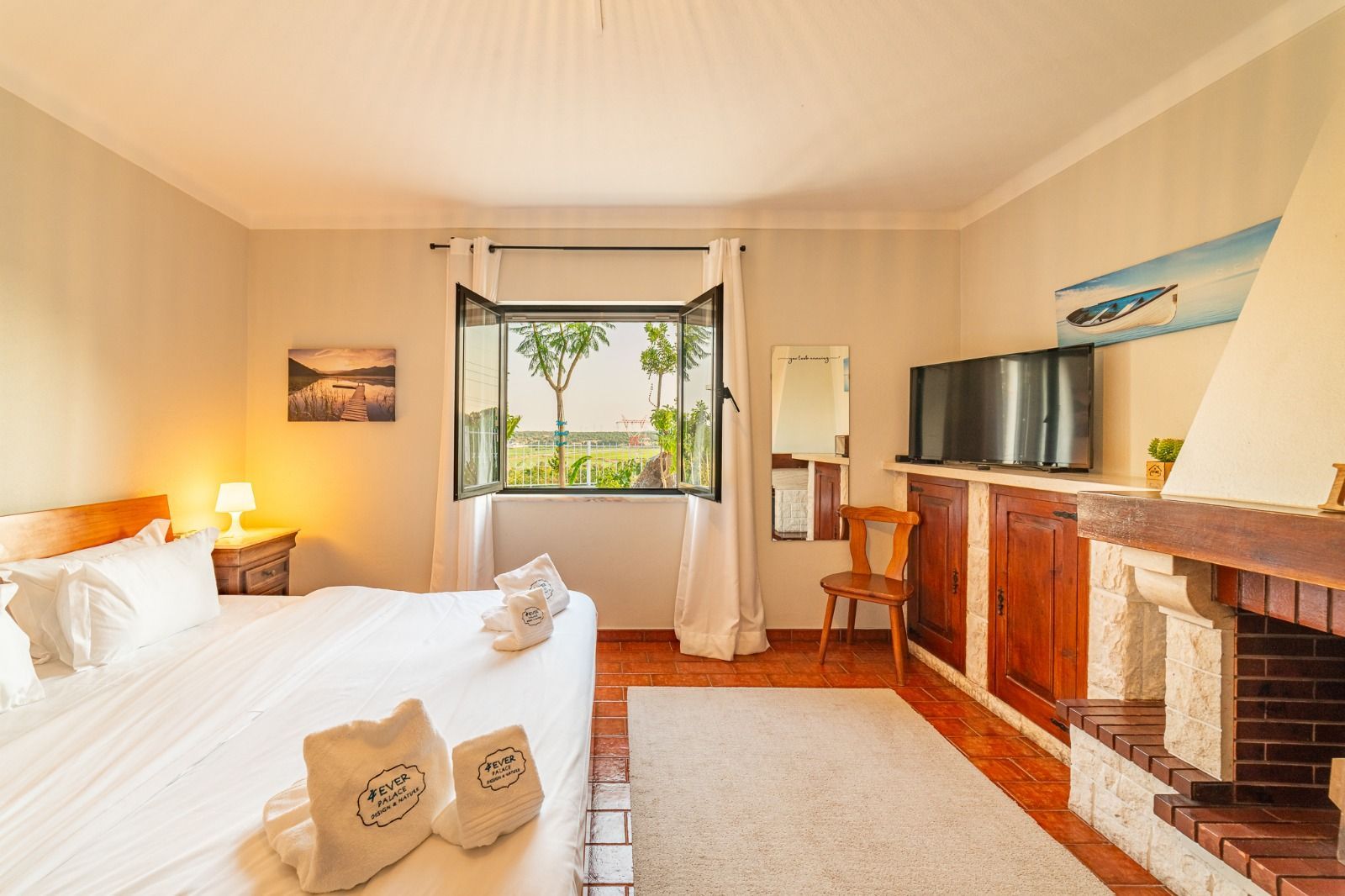 Bright bedroom with two beds, a window view, TV, mirror, and fireplace mantel