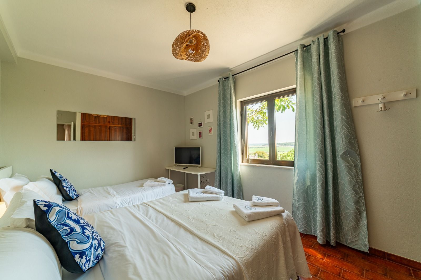 Bright bedroom with a white bed, blue pillows, small desk, window, and teal curtains