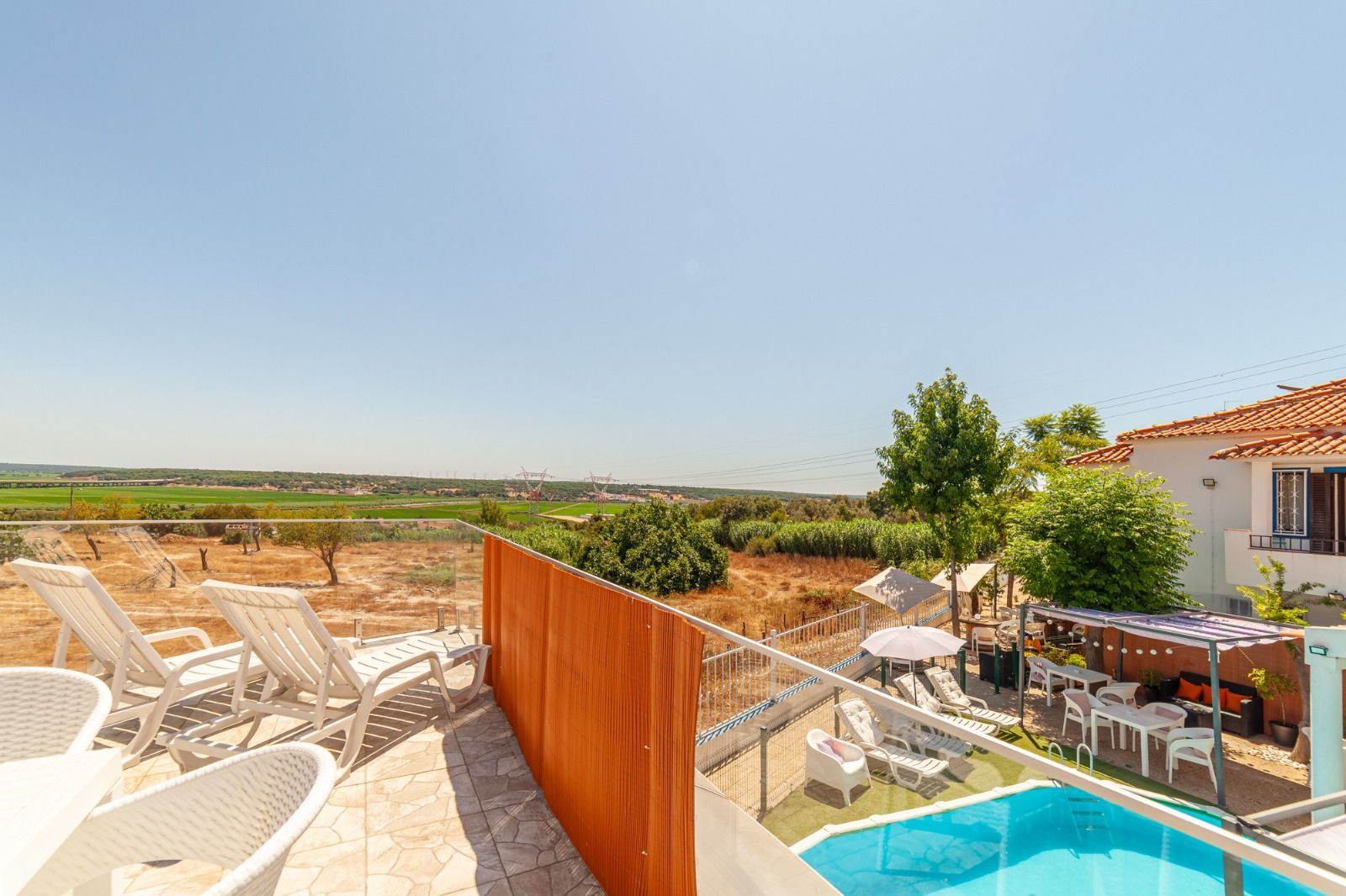 Patio with white lounge chairs, orange divider, small pool, and countryside view under a clear sky