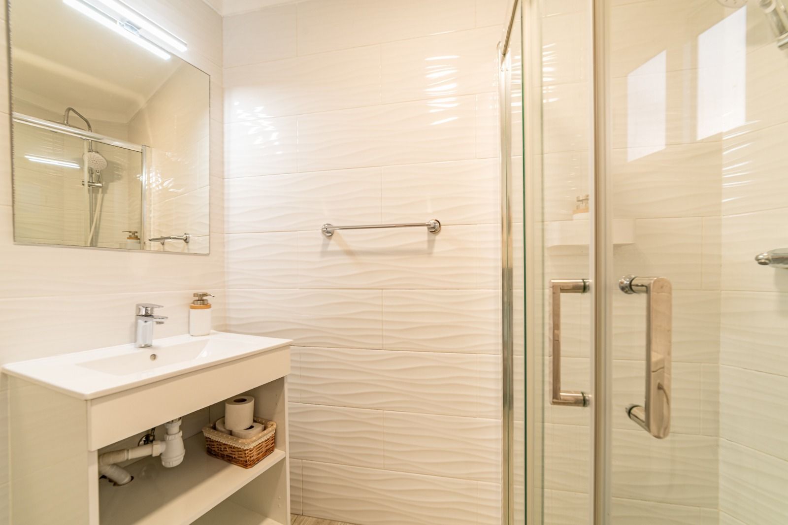 Bright modern bathroom with white tiled shower, glass doors, sink, and wall mirror